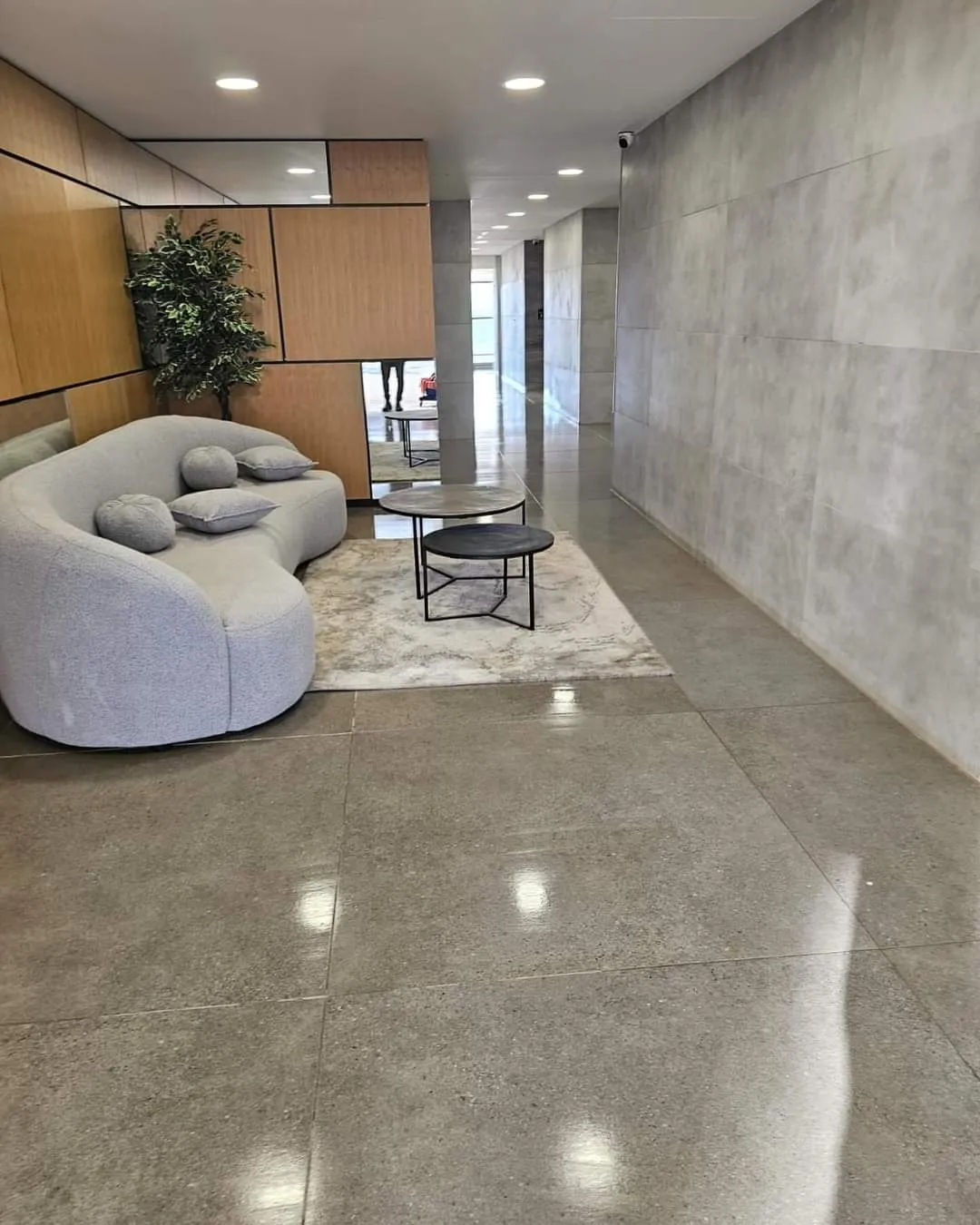 לובי מתוחזק בבניין מגורים בניהול אל ג׳י: פינת ישיבה, רצפה מבריקה וקיר בטון חלק