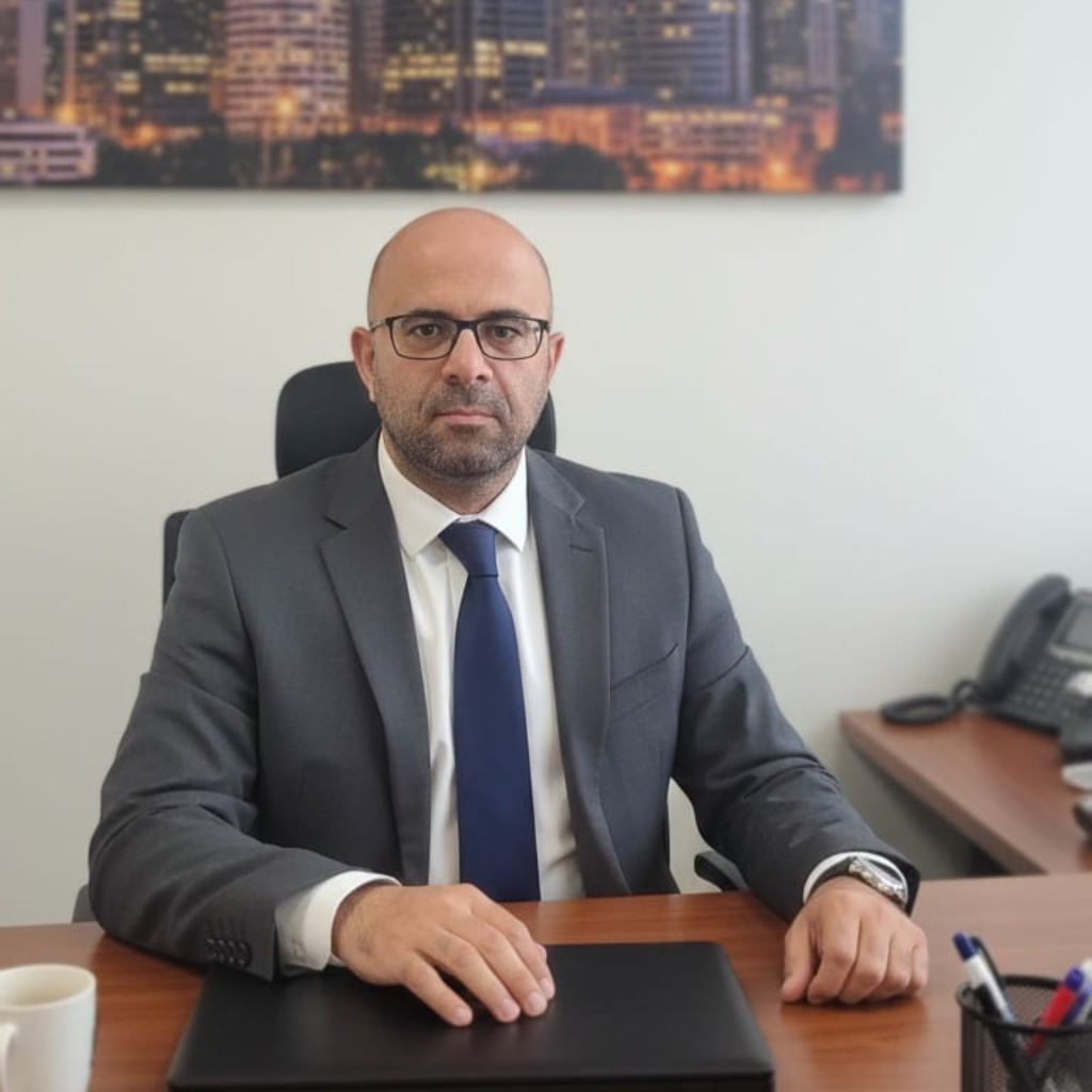 מיכאל אברג'ל יושב במשרד בלבוש עסקי ליד שולחן עבודה